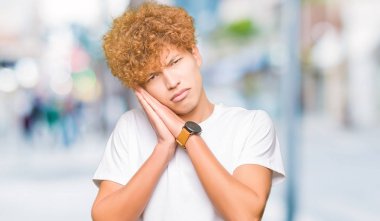 Afro saç ile genç yakışıklı adam rahat beyaz t-shirt uyku yorgun hayal ve el ile poz kapalı gözleri ile gülümseyen süre uyuyan.