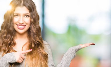 Genç güzel kadın giyiyor Kış Giysi hayret ve gülümseyerek kameraya el ile sunulması ve parmak ile işaret ederken.