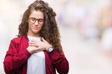 Güzel esmer kıvırcık saçlı Genç kız göğüs kapalı gözlerle ellerinde ve yüzünde minnettar jest ile gülümseyen izole arka plan üzerinde ceket ve gözlük takıyor. Sağlık kavramı.