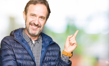 Kameraya bakarak yan el ve parmak ile işaret yüzünde, kocaman bir gülümseme ile kış ceket giyen orta yaş yakışıklı adam.