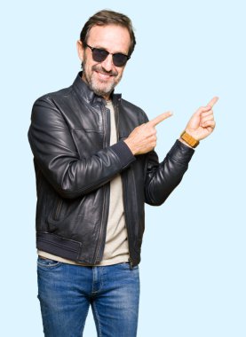 Güneş gözlüğü ve gülümseyen ve iki elleri ve parmakları ile tarafına işaret kamera bakarak siyah deri ceket giyen orta yaş yakışıklı adam.