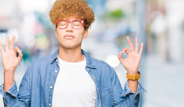 Afro saç ile genç yakışıklı adam gözlük giymek rahatlayın ve gözleri ile gülümseyen meditasyon jest parmaklar ile kapalı. Yoga konsepti.