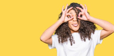 Kıvırcık saçlı beyaz t-shirt giyen genç güzel kadın dürbün yapışır gibi ok jest yapıyor, gözleri parmaklar bakarak. Çılgın ifade.