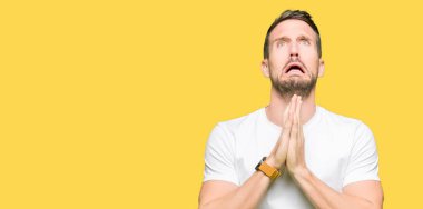 Yakışıklı adam yalvarıyor ve umut ifade yüzünde çok duygusal ve endişe ile birlikte elleriyle dua casual beyaz t-shirt giyiyor. Bağışlanmak. Din kavramı.