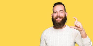 Kış kazak gülümseyen ve boyutu işaret parmaklı ararken ve kamera işi el ile kendine güvenen el hareketi giyen genç hipster adam. Ölçü kavramı.