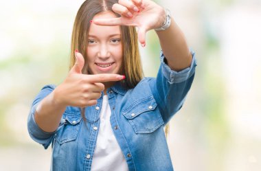 Genç beyaz güzel kadın elle yapma çerçeve ve parmakları ile mutlu yüz gülümseyen izole arka plan yüzünden. Yaratıcılık ve Fotoğrafçılık kavramı.