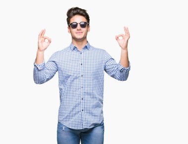 Genç yakışıklı adam giyen güneş gözlüğü izole arka plan üzerinde dinlenmek ve gülümseyen gözlerle parmak ile meditasyon jest yapıyor kapalı. Yoga kavramı.