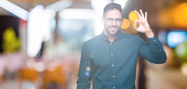 Genç yakışıklı iş adamı izole arka plan el ve parmaklar ok işaretiyle yapıyor olumlu gülümseyen üzerinde gözlük takıyorum. Başarılı ifade.