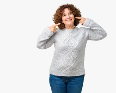 Kendinden emin gösterilen ve işaret parmakları diş ve ağız ile gülümseyen izole arka plan üzerinde kış kazak giyen güzel orta ager üst düzey kadın. Sağlık kavramı.