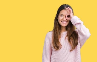 Genç güzel esmer kadın giyiyor pembe kış kazak gülümseyen, parmakları ile mutlu yüz üzerinden seyir göz el ile ok jest yapıyor izole arka plan üzerinde.