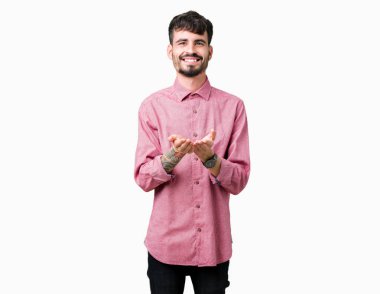 İzole arka planda pembe gömlek giyen genç yakışıklı adam el avuç içi birlikte alma veya jest vererek gülümsüyor. Tutma ve koruma