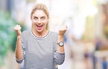 İzole arka plan kutlama üzerinde çizgili süveter giyen genç güzel sarışın kadın şaşırttı ve başarı için kaldırdı kollarını açarak hayret ve gözleri açık. Kazanan kavramı.