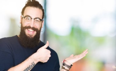 Genç hipster adamım uzun saç ve sakal gözlük ile gösteren palm el ve iş tamam jestle başparmak, mutlu ve neşeli gülümseyen
