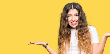 Genç güzel kadın rahat beyaz t-shirt giyen gülümseyerek her iki elaçık avuç içi gösteren, sunan ve reklam karşılaştırma ve denge