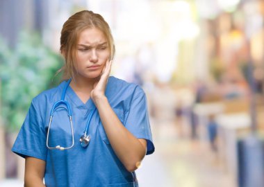 Diş ağrısı veya dişlerde dişlerle ilgili hastalık nedeniyle ağız acı ifadesi ile el ile dokunmak izole arka plan üzerinde cerrah üniforma giyen genç beyaz doktor kadın. Diş hekimi kavramı.