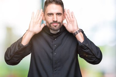 Genç Hıristiyan rahip kulak jest, dedikodu için meraklı her iki ellerde dinliyoruz izole arka plan üzerinde. İşitme sorunu, sağır