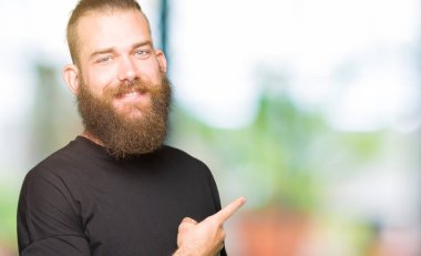 Yüze mutlu ve doğal ifade ile yan kadar el ve parmak ile işaret yüz bir gülümseme ile neşeli rahat t-shirt giyen genç sarışın adam