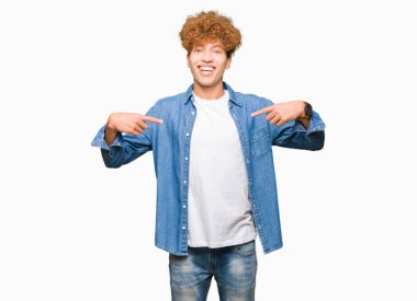 Afro saçlı, kot ceket giyen genç yakışıklı adam yüzünde gülümseme ile kendinden emin görünümlü, parmakları gururlu ve mutlu kendini işaret.