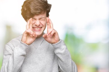 Umut ve gözleri kapalı geçiş parmaklarıyla gülümseyen izole arka plan üzerinde sweatshirt giyen genç yakışıklı sportif adam. Şans ve batıl kavramı.