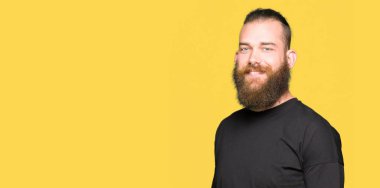 Genç sarışın adam rahat t-shirt üzerinde yüz, doğal ifade gülümseme ile kenara bakıyor giyiyor. Güven gülüyor.