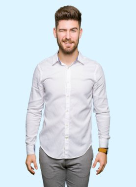 Genç yakışıklı iş adamı seksi bir ifadeyle, neşeli ve mutlu yüzünü kameraya bakarak göz kırpıyor.