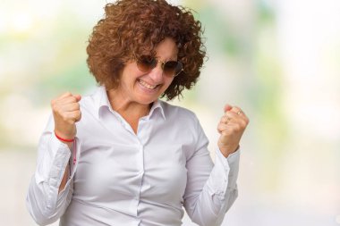 Gülümseyen ve başarı için çığlık izole arka plan çok mutlu ve heyecanlı kaldırdı, silah ile kazanan jest yapıyor üzerinde güneş gözlüğü takıyor güzel orta ager üst düzey bir iş kadını. Kutlama kavramı.