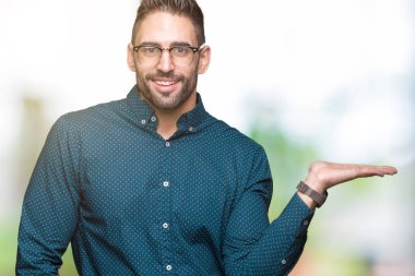 Neşeli sunulması ve kameraya bakarak avucunun ile işaret gülümseyen izole arka plan üzerinde gözlük takan genç yakışıklı iş adamı.