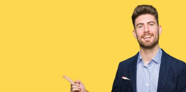 Kameraya bakarak yan el ve parmak ile işaret eden genç yakışıklı bussines adam yüzünde kocaman bir gülümseme ile.