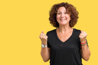 İzole arka plan üzerinde güzel orta ager kıdemli kadın şaşırttı ve silah kaldırdı ve açık gözleri ile başarı için hayran kutluyor. Kazanan kavramı.