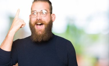 Gözlük ve balıkçı yaka kazak giyen genç sarışın adam başarılı bir fikir ile parmak işaret. Çıkıldı ve mutlu. Bir numara.