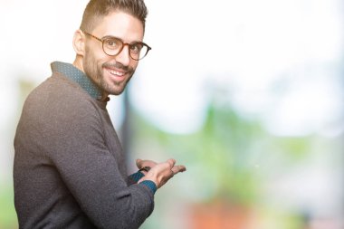 Açık el ile doğal gülümseyen girmek için davet izole arka plan üzerinde gözlük takan genç yakışıklı adam