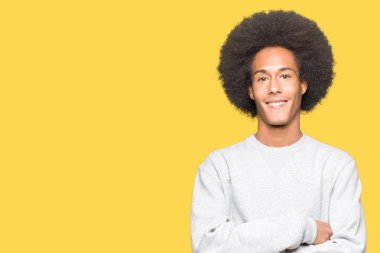 Afrikalı-Amerikalı genç afro saçlı sportif kazak mutlu yüz çapraz silah kameraya bakarak ile gülümseyen giyiyor. Olumlu bir kişi.