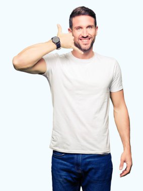 Yakışıklı adam rahat beyaz t-shirt giyen gülümseyen el ve parmak telefonda konuşmak ile telefon jest yapıyor. Kavramları iletişim.