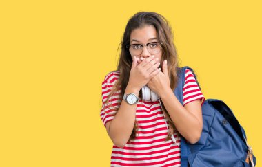 Üzerinde kulaklık ve sırt çantası giyen genç güzel esmer öğrenci kadın arka plan ağız hata için elleriyle kapsayan şok izole. Gizli kavramı.