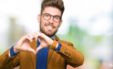 Kalp simgesi ve elleriyle şekil gösterilen aşık gülümseyen gözlüklü genç yakışıklı iş adamı. Romantik kavramı.