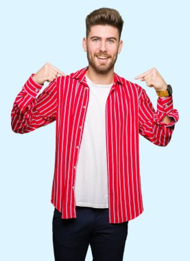 Kırmızı gömlek giyen genç yakışıklı adam yüzünde gülümseme ile kendine güvenen görünümlü, parmaklarıyla gurur ve mutlu kendini işaret.