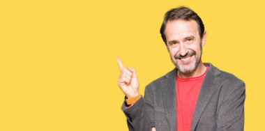 Kameraya bakarak yan el ve parmak ile işaret orta yaş yakışıklı iş adamı yüzünde kocaman bir gülümseme ile.