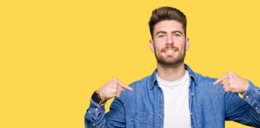 Yüzünde gülümseme ile kendinden emin görünüyorsun, kendini gururlu ve mutlu parmakları ile işaret rahat denim ceket giyen genç yakışıklı sarışın adam.