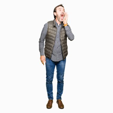 Orta yaş yakışıklı adam kış yelek giyen bağırıyor ve ağız üzerinde el ile yan gürültülü çığlık. İletişim konsepti.