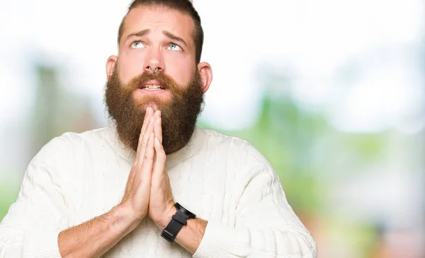 Young hipster man wearing winter sweater begging and praying with hands together with hope expression on face very emotional and worried. Asking for forgiveness. Religion concept.