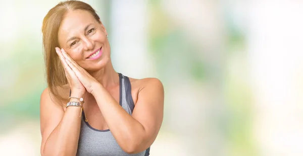 Beautiful middle age woman wearing sport clothes over isolated background sleeping tired dreaming and posing with hands together while smiling with closed eyes.