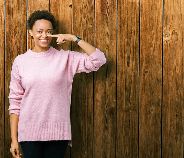 Güzel genç Afro-Amerikan kadın yüzünden izole arka plan işaretçi el parmak yüz ve burun, neşeli gülümseyen