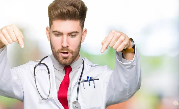 穿着医疗外套的年轻英俊的医生用手指指着广告 惊讶的脸和张开的嘴 — 图库照片