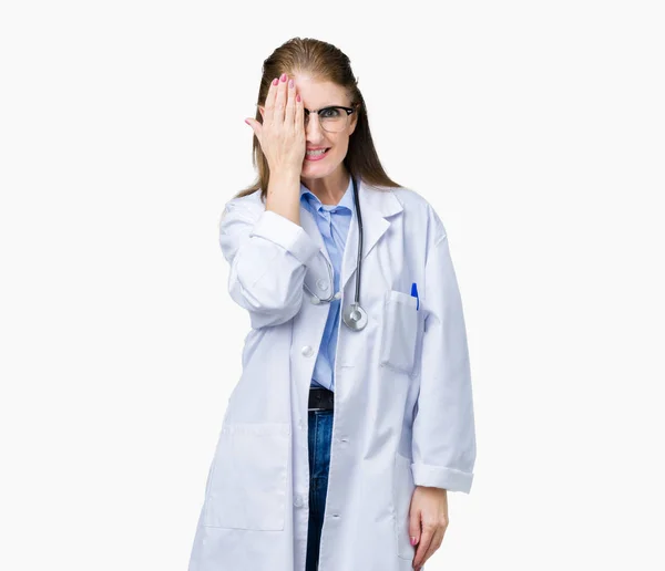 顔と驚きの感情に自信を持って笑顔で手で片目を覆う孤立の背景に医療のコートを着て中年中高年医師女性 — ストック写真
