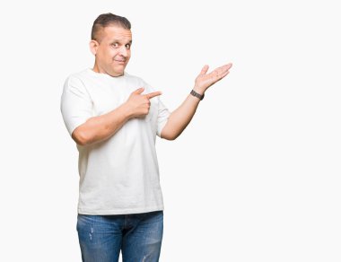 Orta yaş Arap adam wearig beyaz t-shirt üzerine hayrete ve el ile sunulması ve parmak ile işaret ederken kameraya gülümseyen arka plan izole.