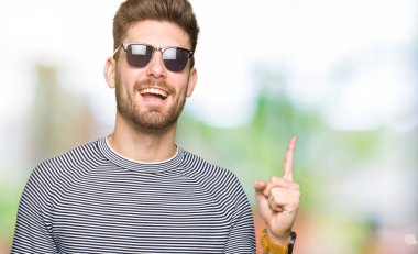 Genç yakışıklı giyen güneş gözlüğü ile başarılı fikir parmak işaret adam. Çıktıktan ve mutlu. Bir numara.