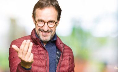 Orta yaş yakışıklı adam gözlük ve kış ceket Beckoning giyen el mutlu ve gülümseyerek davet ile buraya jest gel