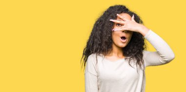 Kıvırcık saçlı genç güzel kız rahat kazak giyen şok yüz ve gözleri el ile kaplayan gözetleme, utanmış ifade ile parmaklarından bakarak.