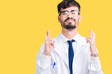 Genç profesyonel bilim adamı adam izole arka plan üzerinde beyaz ceket giyiyor umut ve gözleri kapalı gülümsemek geçiş parmaklar. Şans ve batıl fikir.