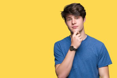 Emin çapraz kollar ve çeneme kaldırdı el ile gülümseme ile kameraya bakarak izole arka plan üzerinde mavi t-shirt giyen genç yakışıklı adam. Pozitif düşünce.